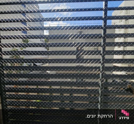רשת מתכת על רקע בניינים ושמיים כחולים